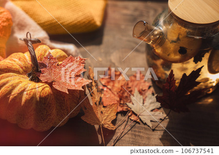 Brewed herbal tea with lemon in a glass teapot next to a pumpkin on a wooden table 106737541