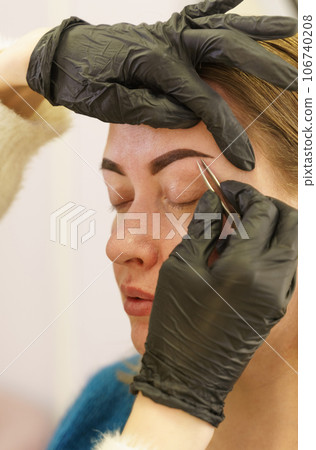 Portrait of a woman having her eyebrows plucked with tweezers in a beauty salon. Beauty industry. Close-up. Vertical frame. 106740208