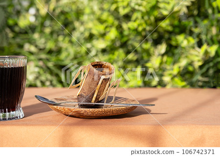 Used drip coffee bag near coffee cup in morning light. Used drip coffee bag near coffee cup in morning light. 106742371