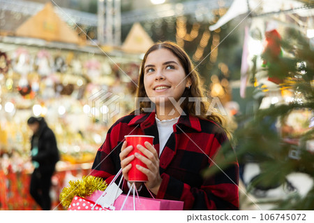 Girl holding paper cup with mulled wine while enjoying a walk through the traditional city street fair on Christmas Eve Girl holding paper cup with mulled wine while enjoying a walk through the traditional city street fair on Christmas Eve 106745072