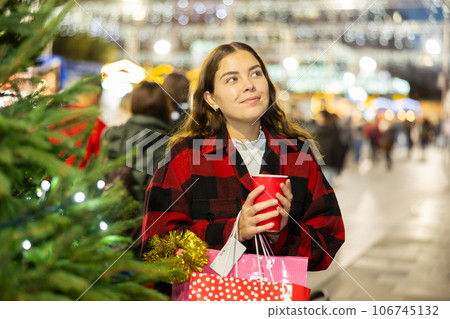 Girl holding paper cup with mulled wine while enjoying a walk through the traditional city street fair on Christmas Eve Girl holding paper cup with mulled wine while enjoying a walk through the traditional city street fair on Christmas Eve 106745132