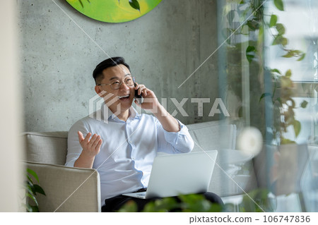 Happy man entrepreneur working sitting on sofa working on laptop and talking mobile phone. 106747836