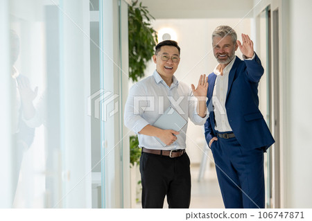 Men walking along corridor in office and talking about their work, waving hands, greeting partners. Men walking along corridor in office and talking about their work, waving hands, greeting partners. 106747871