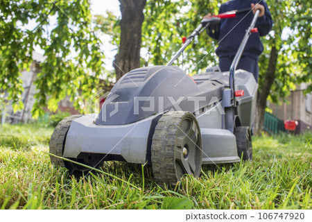 Man with lawnmower is mowing green grass in the garden. Gardening Man with lawnmower is mowing green grass in the garden. Gardening 106747920