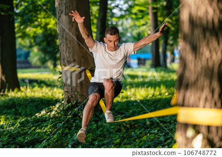 Young guy in sportwear walking on the rope and looking focused Young guy in sportwear walking on the rope and looking focused 106748772