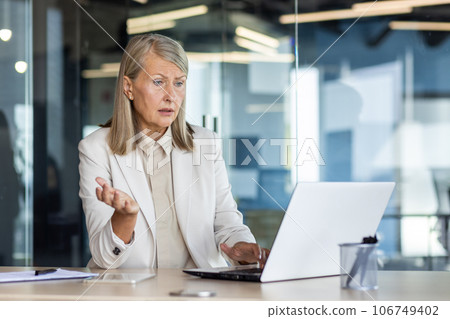 Dissatisfied and disappointed senior gray haired business woman at workplace, female boss received online notification on laptop about poor and unsatisfactory achievement results. Dissatisfied and disappointed senior gray haired business woman at workplace, female boss received online notification on laptop about poor and unsatisfactory achievement results. 106749402