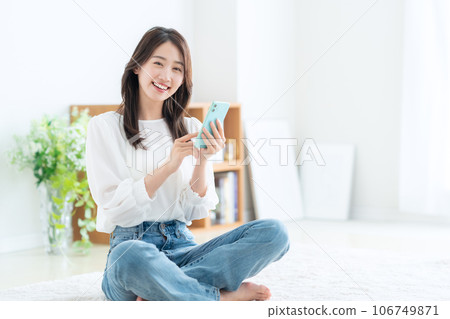 A young woman operating a smartphone in the living room A young woman operating a smartphone in the living room 106749871