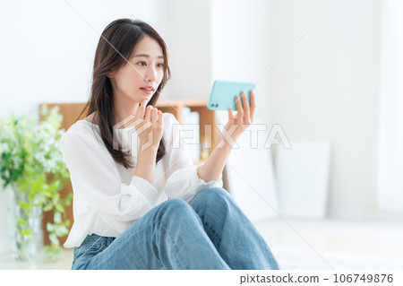 A young woman operating a smartphone in the living room A young woman operating a smartphone in the living room 106749876