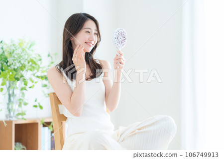 一位年輕女士一邊看著客廳的手鏡一邊做皮膚護理 106749913