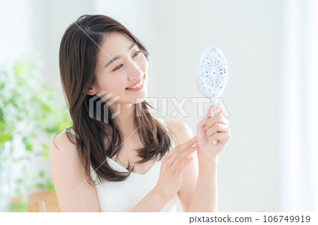 A young woman doing skin care while looking at a hand mirror in the living room 106749919