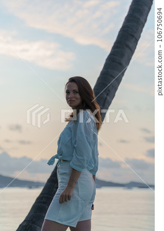 portrait of brunette girl standing at dawn against a palm tree portrait of brunette girl standing at dawn against a palm tree 106750694