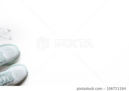 New light blue green female running shoes and headphones on emty white background. Stylish monochrome shoes for active people that incorporate new health technology. Top view 106751384
