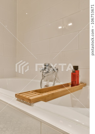 a bathtub with soap and toothbrushs on the edge in a white tiled bathroom wall behind it is a bottle of sham a bathtub with soap and toothbrushs on the edge in a white tiled bathroom wall behind it is a bottle of sham 106753671