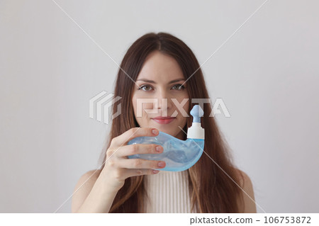 A young woman demonstrates the Neti Pot for treating runny nose and colds. Nasal rinsing, irrigation therapy. 106753872