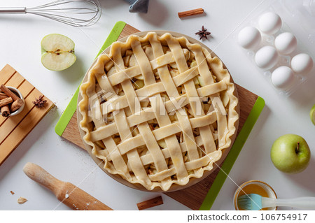 Uncooked apple pie into a baking dish ready for cooking on a white table surrounded by ingredients 106754917