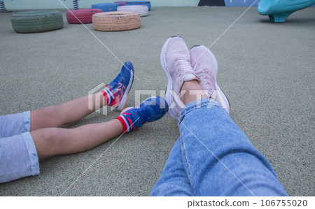 legs on woman and her child sitting on the ground on the playground.top view . legs on woman and her child sitting on the ground on the playground.top view . 106755020