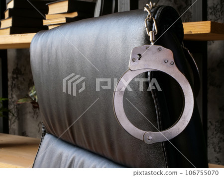 Handcuffs on the back of office chair as a concept for financial crimes or bribery. Handcuffs on the back of office chair as a concept for financial crimes or bribery. 106755070