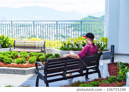 Young tourist man resting on the bench and looking at Nha Trang city Young tourist man resting on the bench and looking at Nha Trang city 106755286