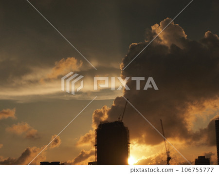 A sunset scene in Kaohsiung City, southern Taiwan, with the setting sun, a silhouetted skyscraper under construction, and a crane stuck in the clouds. 106755777