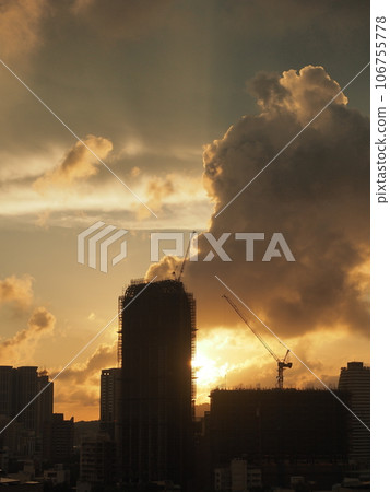 Vertical composition, sunset scene in Kaohsiung City in southern Taiwan, cumulonimbus clouds illuminated by the setting sun, and rays of light coming from silhouetted skyscrapers. 106755778