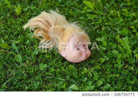 A doll's head with spoiled blond hair, discarded in a park meadow. 106756773
