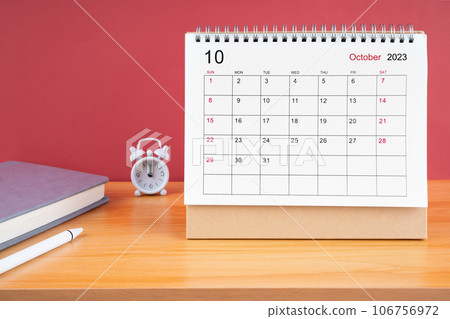 The October Monthly desk calendar for 2023 year and alarm clock on wooden table. 106756972