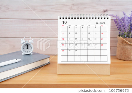 The October Monthly desk calendar for 2023 year and alarm clock on wooden table. 106756973
