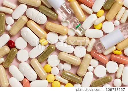 Mix of medical capsules and pills on light pink top view. Medicinal treatment 106758337