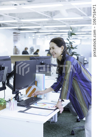 Senior business woman reaching for a laptop, vertical position Senior business woman reaching for a laptop, vertical position 106758471