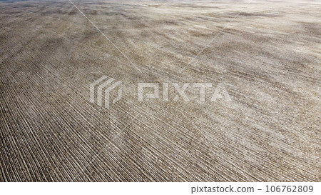 From above, the view captures a plowed farm field against a canvas of deep black soil. From above, the view captures a plowed farm field against a canvas of deep black soil. 106762809