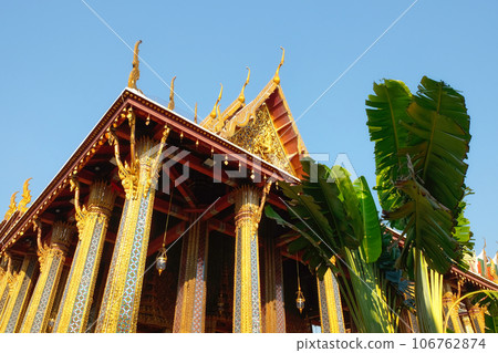 A grand temple, adorned with gilded columns and a crimson roof, rises gracefully amid lush greenery, set against a backdrop of an unblemished azure sky. A grand temple, adorned with gilded columns and a crimson roof, rises gracefully amid lush greenery, set against a backdrop of an unblemished azure sky. 106762874