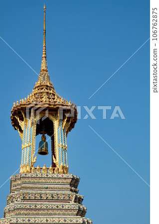 An ornate Thai temple bell tower with a golden roof and colorful details, stands against a clear blue sky. 106762875