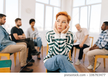 Portrait of pensive young woman covering ears with hands and looking away sitting in circle at group psychological counseling. Concept of mental health, psychotherapy, social issues, support. Portrait of pensive young woman covering ears with hands and looking away sitting in circle at group psychological counseling. Concept of mental health, psychotherapy, social issues, support. 106763477