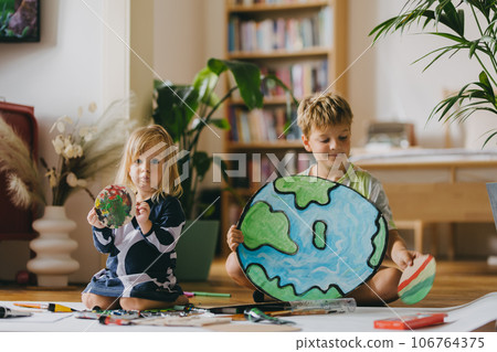 Siblings painting at home with watercolors and tempera paints, creating a model of planet Earth. Siblings painting at home with watercolors and tempera paints, creating a model of planet Earth. 106764375