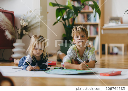 Siblings lying on stomach and painting at home with watercolors, markers and tempera paints, creating a model of planet Earth. 106764385