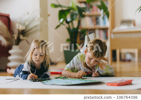 Siblings lying on stomach and painting at home with watercolors, markers and tempera paints, creating a model of planet Earth. 106764386