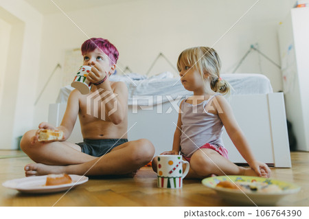 Siblings sitting on the floor and having a snack in their children's room. Siblings sitting on the floor and having a snack in their children's room. 106764390