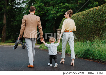 Young family with little son on walk in city park after work. Young family with little son on walk in city park after work. 106764461