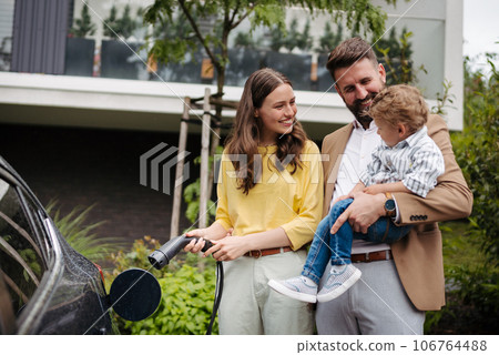 Happy family standing beside their car and charging electric car on the street. 106764488