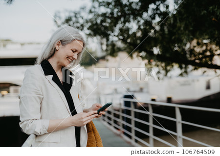 Portrait of beautiful woman with gray hair in city, using her smartphone. Portrait of beautiful woman with gray hair in city, using her smartphone. 106764509