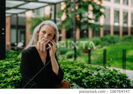 Portrait of a beautiful woman with gray hair making a call outdoors. 106764547
