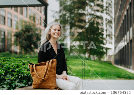 Portrait of beautiful woman with gray hair sitting on bench in city. Portrait of beautiful woman with gray hair sitting on bench in city. 106764553