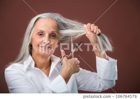 Portrait of senior woman cutting own gray hair. 106764579