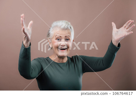 Portrait of smiling senior woman with raised arms in studio. 106764617