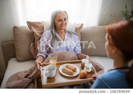 Nurse serving food in the bed to a lying patient at her home. Nurse serving food in the bed to a lying patient at her home. 106764644