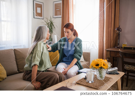 Thoughful nurse examining senior patient with stethoscope at her home. Thoughful nurse examining senior patient with stethoscope at her home. 106764675