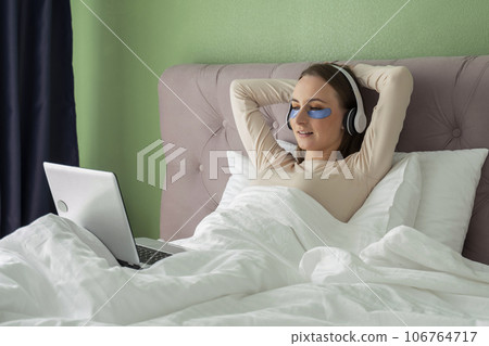 Woman lying in bed listening to music, audiobook, podcast, enjoying meditation for sleep and peace of mind in wireless headphones. 106764717
