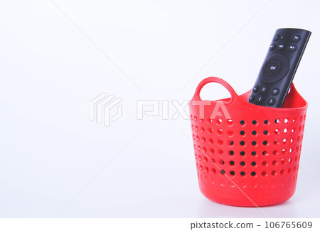 The TV remote is in the trash. Full red trash can. 106765609