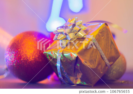 New Year's gift in a bright package against the background of Christmas decorations and bright lights of the garland. 106765655