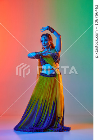 Odissi dance. Beautiful young woman in traditional dress dancing against gradient studio background in neon light 106766462